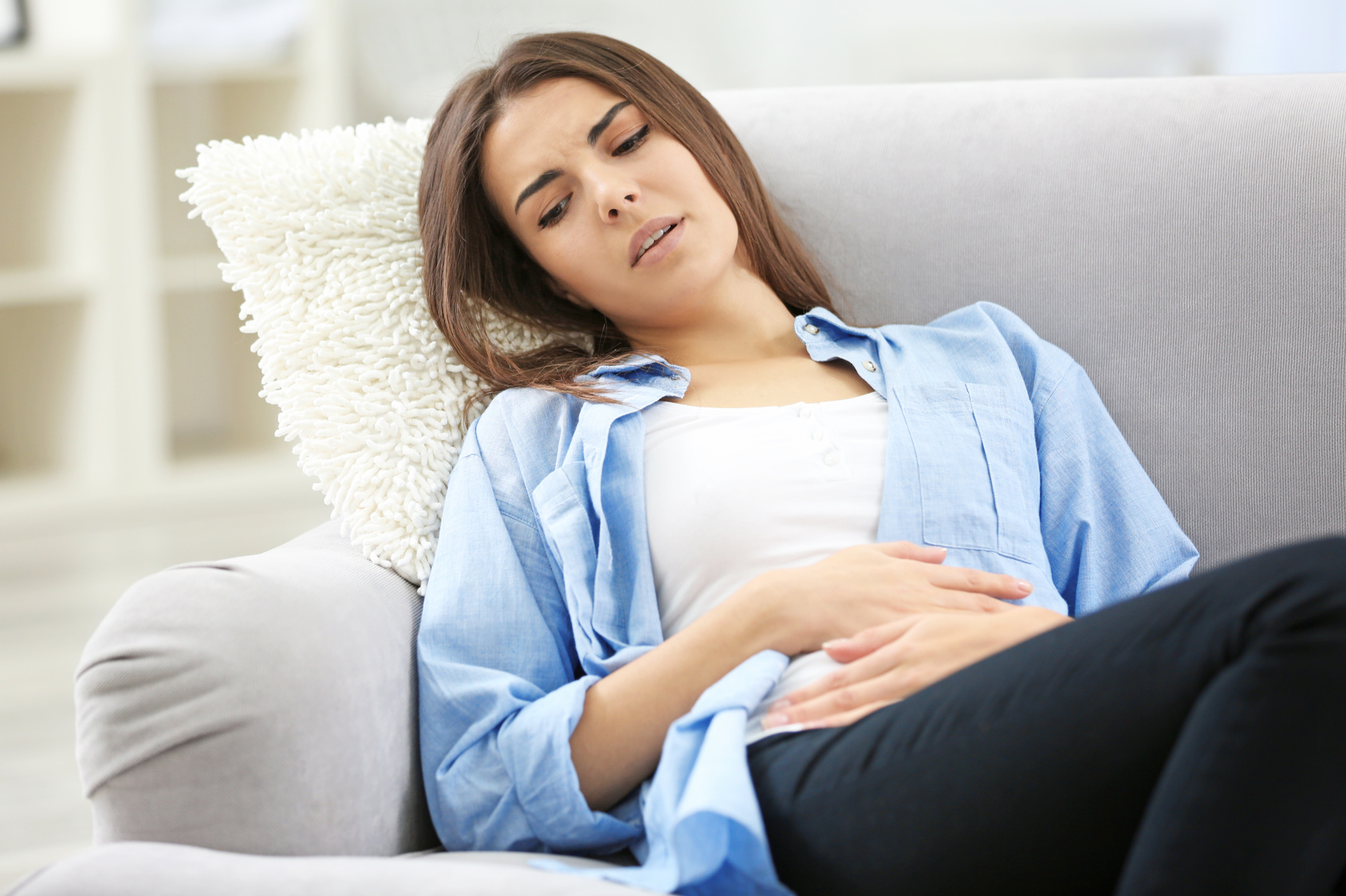 Frau hält sich den Bauch und liegt auf einem Sofa