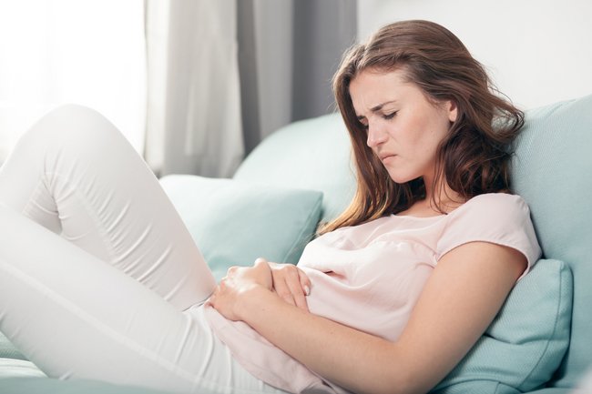 Frau sitzt auf einer Couch und hält sich den Unterleib