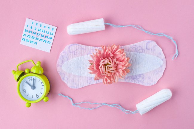 Wecker, Kalender, Tampons und Binde auf rosa Untergrund